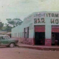 Imagem paisagem de um esquina de um bar. Na frente do estabelecimento tem um carro verde.