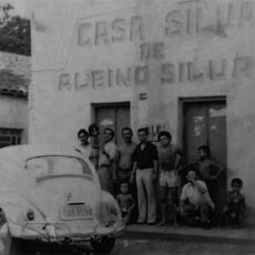 Imagem de um grupo de pessoas em frente do estabelecimento, próximo do grupo há um fusca claro. Na parte de cima do estabelecimento é possível ler "Casa Silva de Albino Silva"