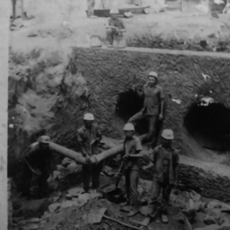 Imagem (retrato/PB) mostrando um buraco fundo com 4 homens todos com equipamento de segurança.